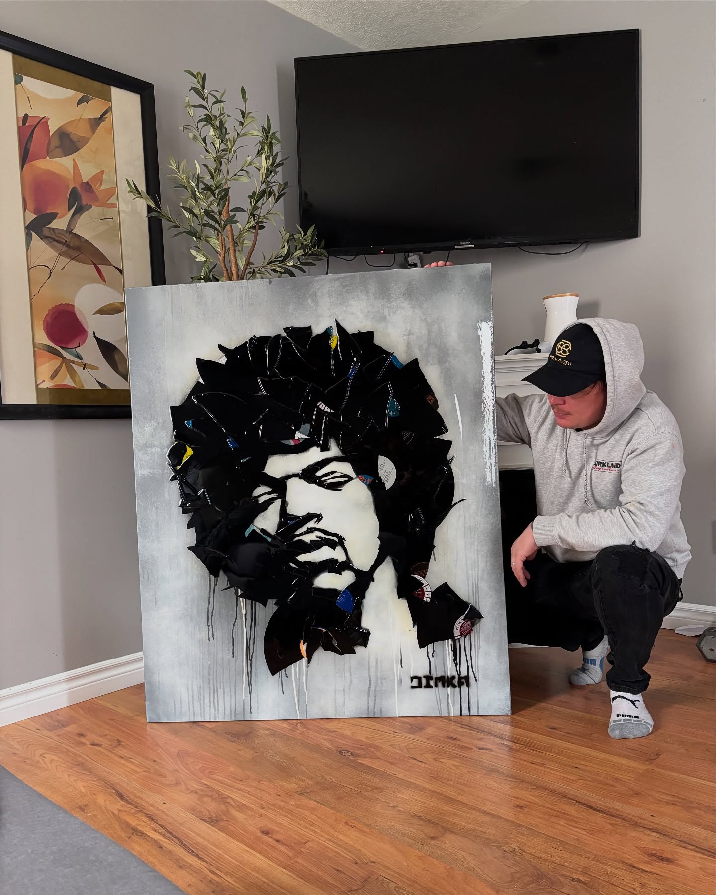 Dimka kneeling beside his Jimi Hendrix portrait with broken vinyl records forming the hair